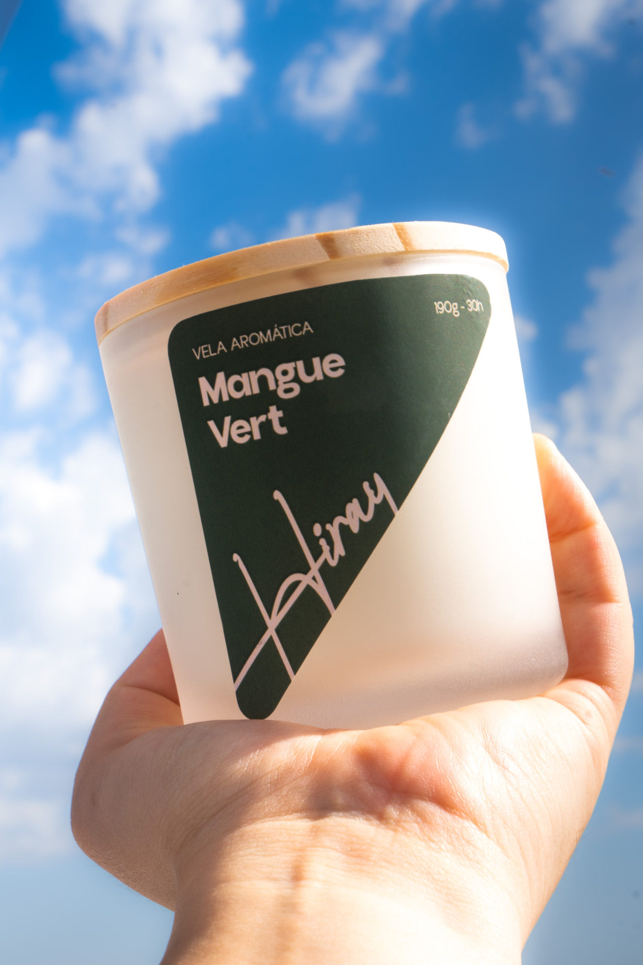 Vela Aromática Mangue Vert Hiray segurada contra o céu azul